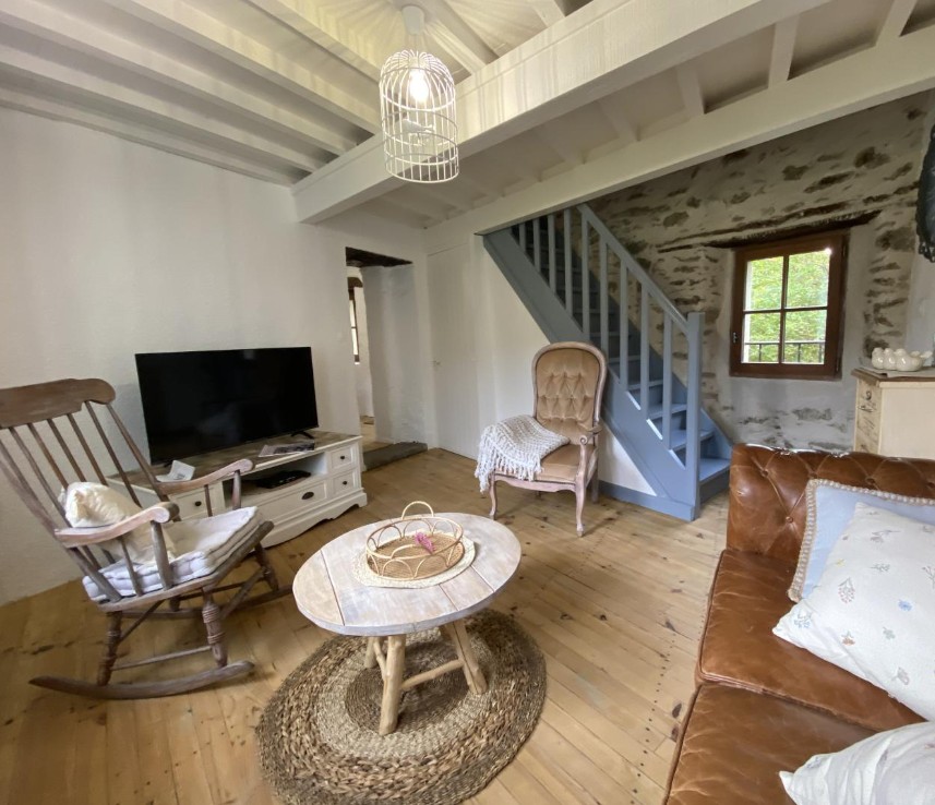 Salon chaleureux du gîte avec rocking chair, escalier bleu et poutres apparentes
