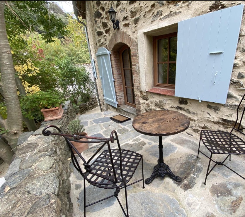 Terrasse avant en pierres avec table bistrot et volets bleus